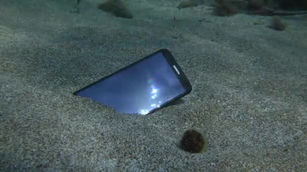 Raggi di sole riflessi dallo schermo di uno smartphone Huawei smarrito sdraiato su un fondo sabbioso. — Video Stock