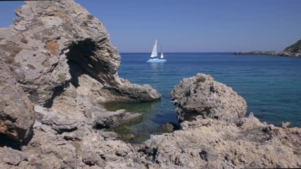 Paisaje marino mediterráneo, pintorescos acantilados de una tranquila bahía, al fondo un yate de vela. — Vídeos de Stock