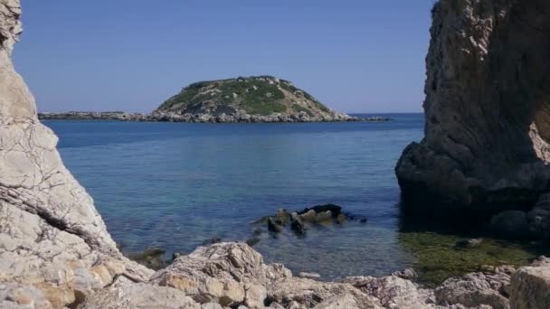 Paisaje marino mediterráneo, una pequeña isla cerca de la costa enmarcada por rocas volcánicas. — Vídeos de Stock