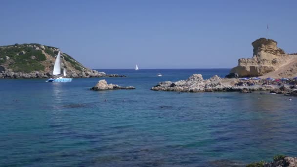 Середземноморський морський ландшафт, купання туристів, вітрильна яхта на фоні мальовничого скелястого острова.. — стокове відео
