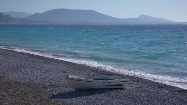 Un bateau sur le rivage sur fond de mer turbulente et de montagnes lointaines. — Video