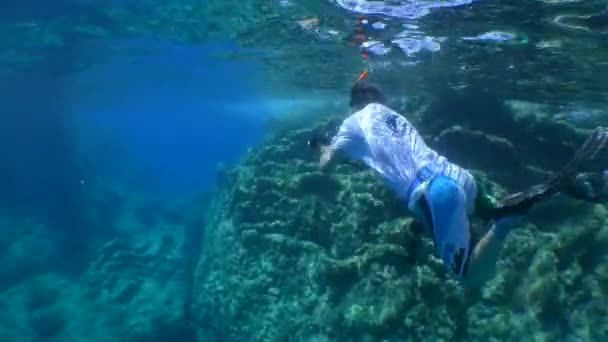 Um freediver com uma câmera nada longe ao longo de um penhasco costeiro rochoso. — Vídeo de Stock