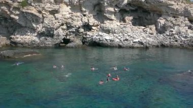 Şnorkelle yüzme: bir grup turist, kayalık bir kıyıya karşı sualtı maskesi takıyor..