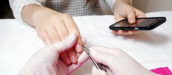 Woman is getting manicure service and using smartphoe  in a salon — Stock Photo, Image