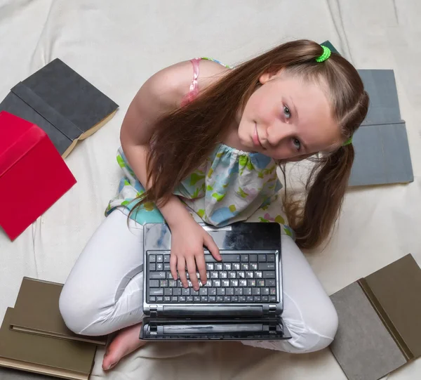 Una niña está estudiando con el ordenador portátil y los libros alrededor de su v superior — Foto de Stock