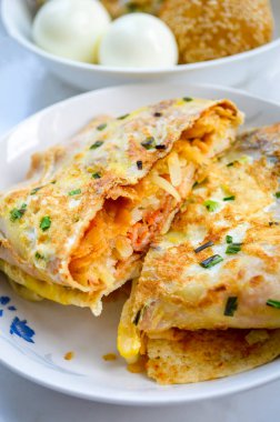 Çin kahvaltısı (Jian Bing) pastırma ve patates iplikleriyle doldurulmuş yumurtalı kek. Arka planda yumurtalar bulanık.