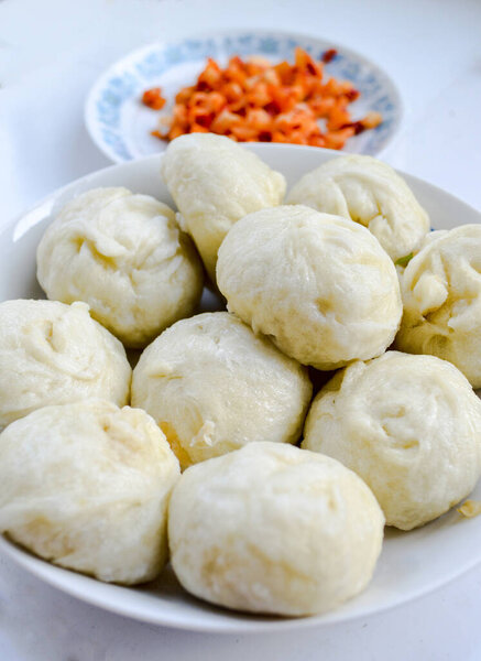 Китайские краденые булочки, баоцзы, популярный завтрак в Китае. Маринованный овощ с красным чили размыт на заднем плане.