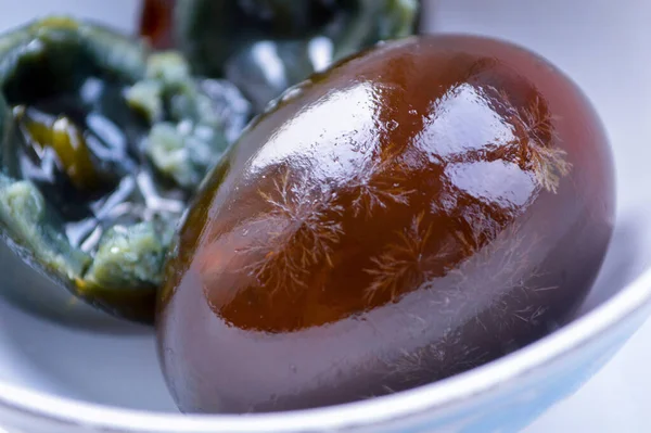 Beyaz kasedeki Çin yüzyıl yumurtalarına yakın çekim. Yumurtanın beyazı yarı saydamdır ve kar tanelerinin desenlerini gösterir. Arka plan, içinde siyah yumurta sarısı olan bulanık bir yarım yumurta gösteriyor..