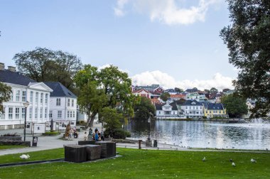 Stavanger, Norveç, 6 Haziran 2025. Stavanger şehir merkezinde ağaçların ve renkli evlerin yansımasıyla huzurlu bir göl.. 