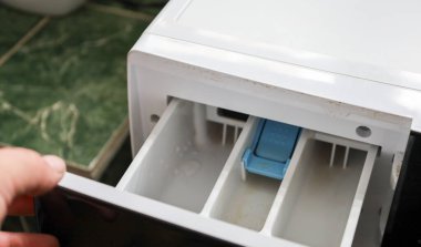 Bu yakın çekim deterjan ve yumuşatıcı için tasarlanmış çamaşır makinesinin çekmecesini açan bir eli gösteriyor..