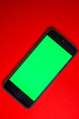 This minimalistic shot shows a smartphone with a chromakey (green) screen, positioned diagonally on a saturated red background.