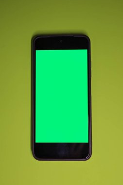 This vertical minimalistic shot showcases a smartphone with a bright green chromakey screen, centrally positioned on a lime or chartreuse background.