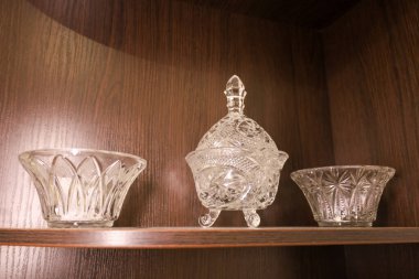 An elegant collection of crystal glassware, consisting of a central candy dish on legs and two side bowls, adorns a dark wooden shelf.