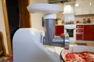 This close-up shot focuses on the metal part of the electric meat grinder, from which the last portion of crushed tomato is emerging