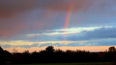 Canlı bir gökkuşağı, ılık altın-pembe tonlarda sakin akşam gökyüzünü kaplayarak gerçeküstü ve büyülü bir atmosfer yaratır. Alacakaranlığı aydınlatan doğal bir mucize.