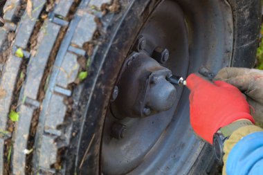 Kırmızı eldivenli bir elin basıncını kontrol ettiği ya da merkezdeki vanadan lastiği şişirdiği derin bir tarımsal lastiğin yakın çekimi..