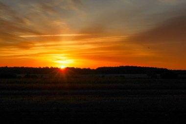 İnanılmaz derecede parlak bir güneş doğar ya da batar, ufuk çizgisinin üzerinde göz kamaştırıcı yıldız ışınları saçar. Gökyüzü turuncu ve altının zengin tonlarıyla alevler içinde, dramatik ve ateşli bir atmosfer yaratıyor..