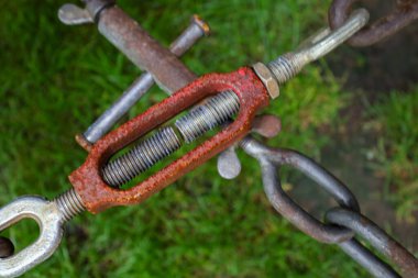 Kırmızı, paslı gövdeli, metal zincir halkalarını bulanık yeşil çimenli arka plana bağlayan endüstriyel bir paraşütün yakın çekimi. Nesne gücü, gerilimi, güvenli bağlanmayı, inşaatı ve ağır iş mühendisliğini simgeliyor..