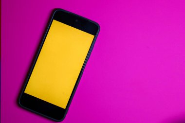 Parlak sarı ekranlı dikey odaklı bir akıllı telefon zengin bir mora dayanır. Minimalist kompozisyonda, temiz ekran, kopyalama alanı veya tasarım modeli olarak kullanmak için ideal bir mobil aygıt gösterilir.