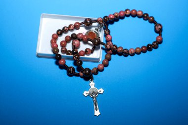 Doğal pembe ve kahverengi taştan boncuklu iki dini bilezik, bir metal haç ve bir madalyon parlak mavi bir arka plana yerleştirilir..