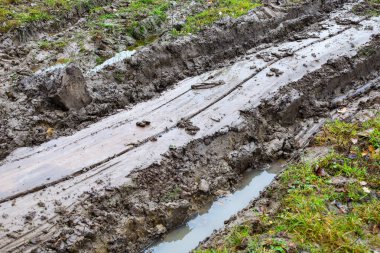 Çamurlu bir köy yolunda suyla dolu derin monotonlukları gösteren yakın çekim bir görüntü, desenli ve ıslak bir görünüm yaratıyor. Görüntü zorlu off-road koşulları ve pürüzlü, geçilemez araziyi aktarıyor.