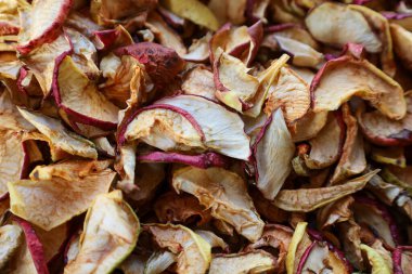 Yoğun bir yakın çekim, kaotik bir yığın içinde uzanan büyük miktarda kurutulmuş elma dilimlerini gösterir, sarı, kırmızı ve kahverengi tonlarda zengin bir doğal doku yaratır..