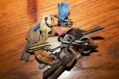 Bir sürü eski, yıpranmış metal tuş, birkaç metal halkayla bir arada tutulan ahşap bir yüzey üzerinde duruyor. Anahtarların arasında eski kumaş parçaları var, mavi ve turuncu-kahverengi, bağbozumu ve unutulmuş görünümü arttırıyor. . 