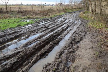 Kırık toprak bir yol, derin, çamurlu bir karışıklığa dönüştü su dolu rutinler, ufuktaki tarım alanlarına doğru uzanıyor..