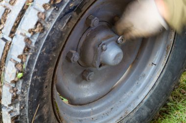 Yakın çekim büyük, kirli bir lastik ve eski, gri bir tekerlek merkezini gösteriyor. Tekerlek cıvataları ve merkezi kapak çıkarılabilir gibi görünüyor..
