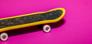 Parlak sarı kenarı ve siyah pürüzlü ayak yüzeyi olan minyatür bir klavye (mini kaykay) doymuş parlak morumsu bir arka plan üzerinde çapraz konum alır..