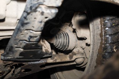 Kirli bir arabanın ön süspansiyonunu ve tekerlek çekiş bileşenlerini gösteren yakın çekim görüntüsü, sabit-hız (CV) ekleminin lastik çizmesi ve bir kontrol kolu.