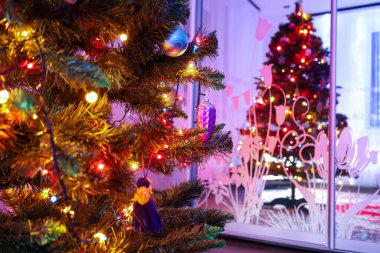 Parlak ışıklandırılmış bir Noel ağacının yakın çekimi. Renkli süsler ve parıldayan ışıklar var. Şenlikli bir odak noktası oluşturuyor..