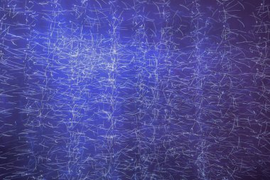 Binlerce kaotik beyaz ve açık mavi ışık çizgisi ile kaplı koyu mor-mavi arkaplanda soyut bir kompozisyon. Görüntü bir enerji akışına, yıldız tozuna ya da dijital veri görselleştirmesine benzer.. 