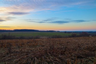 Uçsuz bucaksız bir sonbahar tarlası kuru otlarla kaplı sonsuz bir akşam gökyüzünün altında gün batımının yumuşak ışığının derin mavi ile buluştuğu yerde..