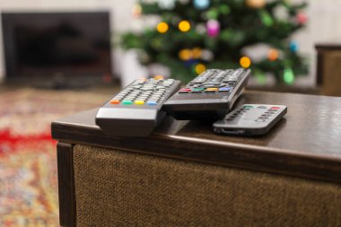 Oturma odasındaki bir koltuğun ahşap koltuğunda bir sürü uzaktan kumanda var. Televizyon izlemek için hazırlanıyorlar..