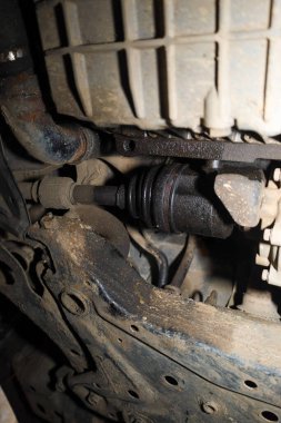 CV ekleminde ve motor yağı tavasında açık yağ sızıntısı belirtileri olan araba şasisinin görüntüsü. Aracın süspansiyon ve şanzımanının teknik durumu, sıvı kirliliği ve metal elementlerin aşınması nedeniyle onarım gerektirmektedir..