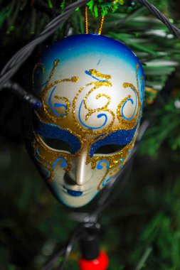 Mavi ve altın desenli Venedik tarzı zarif bir dekoratif maske, çam dalları arasında bir Noel ağacını süslüyor..