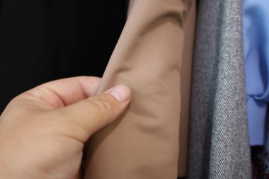 Bir insan eli yumuşak bej kumaşa dokunur, bir mağazada ya da gardıropta yumuşak dokusunu ve yüksek malzeme kalitesini gösterir..