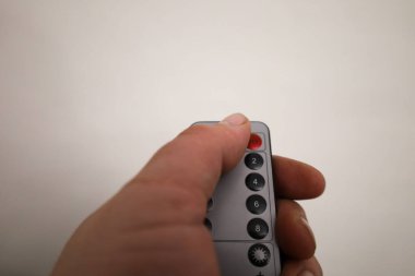 Bir adamın eli, hafif nötr arkaplana karşı gri bir uzaktan kumanda tutarak düğmeye basmaya hazırlanıyor..