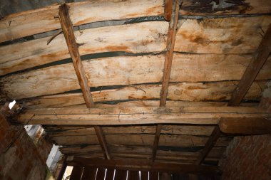 Terk edilmiş bir binanın kaba ahşap tavanı düzensiz kalaslardan ve uzun vadeli çürüme belirtileriyle dolu devasa kirişlerden oluşur..
