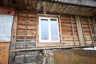 Yeni monte edilmiş modern plastik pencereli eski bir ahşap kulübenin dış cephesi. Duvarlarda sürmekte olan yenileme işaretleri var. Pencere çerçevesinde köpük ve ahşap kaplamalar da dahil.,