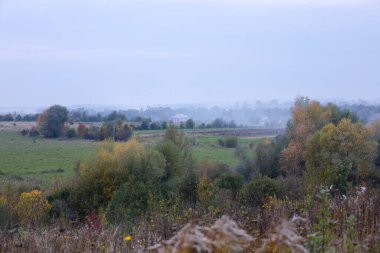 Sonbahar vadisinin panoramik manzarası sabah sisi ile kaplanmış engin çayırlar ve renkli ağaçlarla. Kasvetli bir günde sakin bir kırsal bölge doğadaki mevsimsel değişimler sırasında sessizlik ve doğal uyum atmosferini taşır..