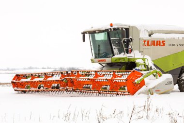 Lviv, Ukrayna - 07 Ocak 2026: Parlak turuncu Maxflex başlıklı güçlü bir Claas Lexion 580 tahıl biçme makinesi karlı bir kış tarlasının ortasında duruyor.