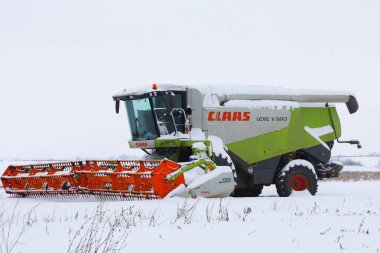 Lviv, Ukrayna - 07 Ocak 2026: Makinelerin parlak turuncu başlığı ve yeşil gövdesi, modern tarım ekipmanlarının ölçeğini vurgulayarak beyaz ufka karşı çelişkili bir aksan oluşturuyor.