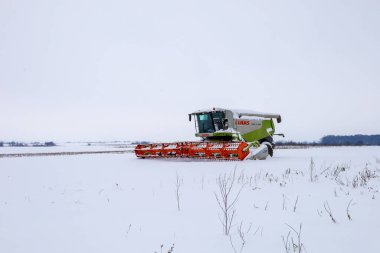 Lviv, Ukrayna - 07 Ocak 2026: Claas Lexion, bulutlu bir kış gökyüzü altında geniş bir kar tarlasının ortasında hasatçıları birleştirdi.