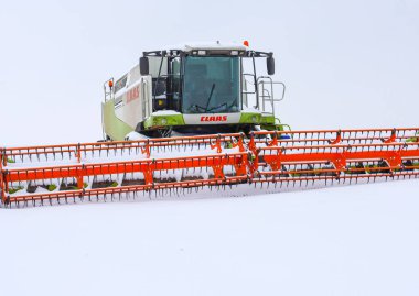 Lviv, Ukrayna - 07 Ocak 2026: Claas Lexion 'un güçlü taksisi ve turuncu başlığı donmuş bir tarlanın ortasında taze karla kaplıdır..