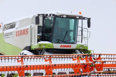 Lviv, Ukrayna - 07 Ocak 2026: Bir Claas Lexion 'un güçlü taksisi ve parlak turuncu başlığı donmuş bir kış tarlasının ortasında taze karla kaplanmıştır..