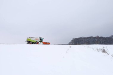 Lviv, Ukrayna - 07 Ocak 2026: Yeşil bir Claas hasat makinası, kasvetli bir kış gökyüzünün altında, engin bir kar örtüsü altında duruyor..