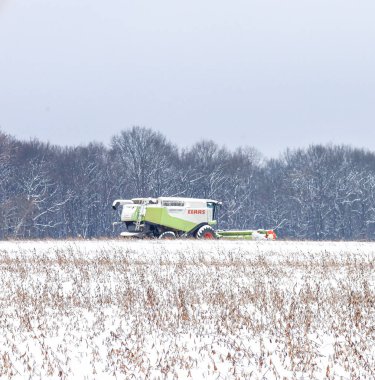 Lviv, Ukrayna - 7 Ocak 2026: Modern bir Claas Lexion hasat makinası, hasat sezonunun sonlarına doğru karla kaplı bir tarlada çalışır..