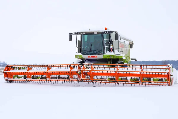 Lviv, Ukrayna - 07 Ocak 2026: Güçlü bir Claas Lexion, kış uykusunda karlı bir tarlanın ortasında parlak turuncu bir başlıkla hasatçıyı birleştirdi.